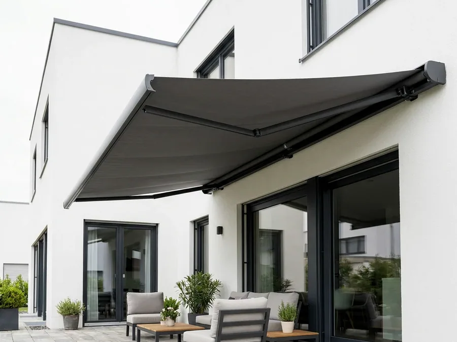 Folding-arm awning extended over a patio, its fabric canopy carried on articulated arms off the house wall