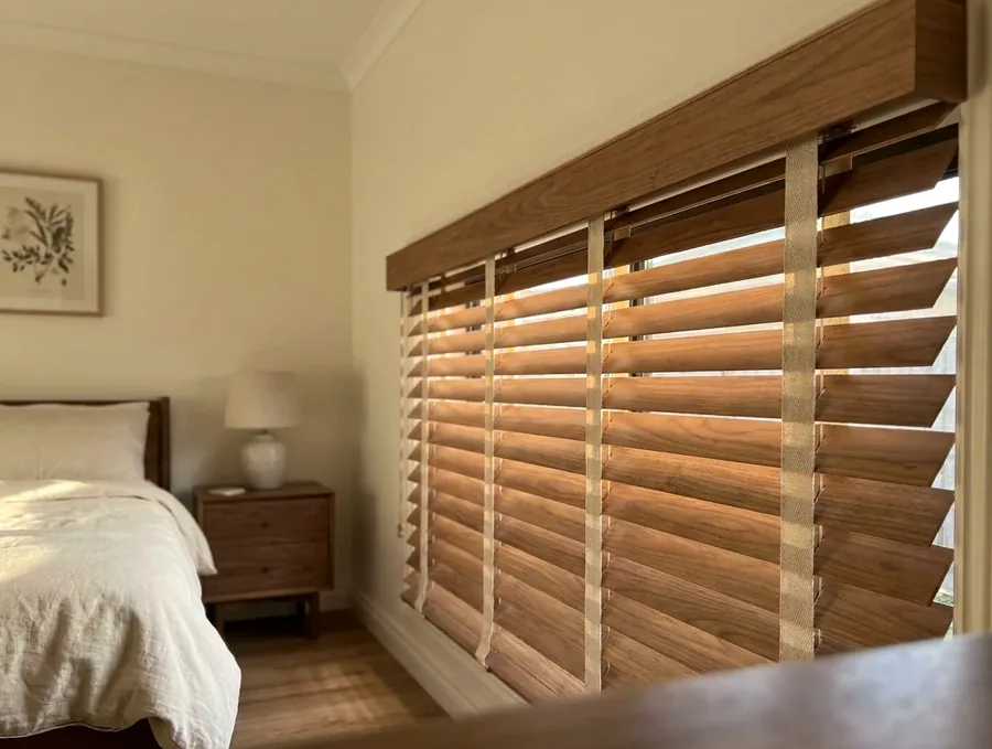 Timber venetian blind with 50mm basswood slats and woven ladder tapes, fitted under a matching timber pelmet in a bedroom